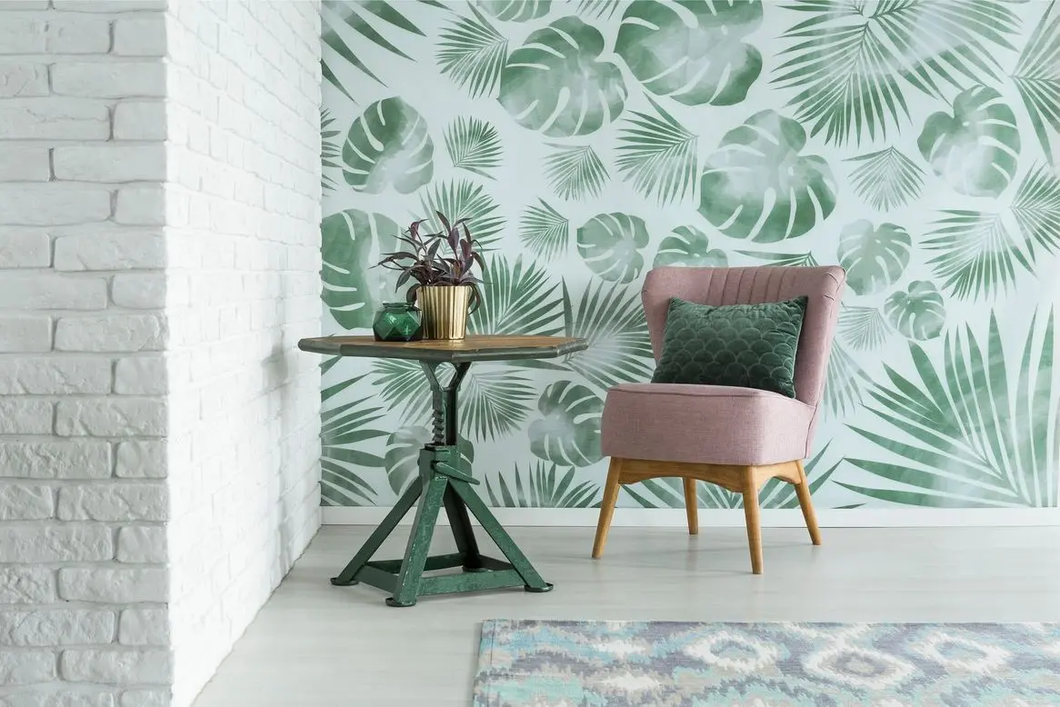 Green pillow on pink chair next to a table with plant in gold pot in room with floral wallpaper and brick wall by Frederick Painting in Frederick, MD