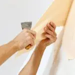Man in with a scraper in the process of removing old wallpaper.
