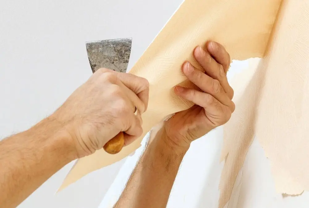 Man in with a scraper in the process of removing old wallpaper.