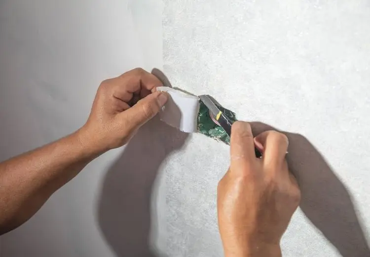 Worker cutting wallpaper near socket box to the wall.