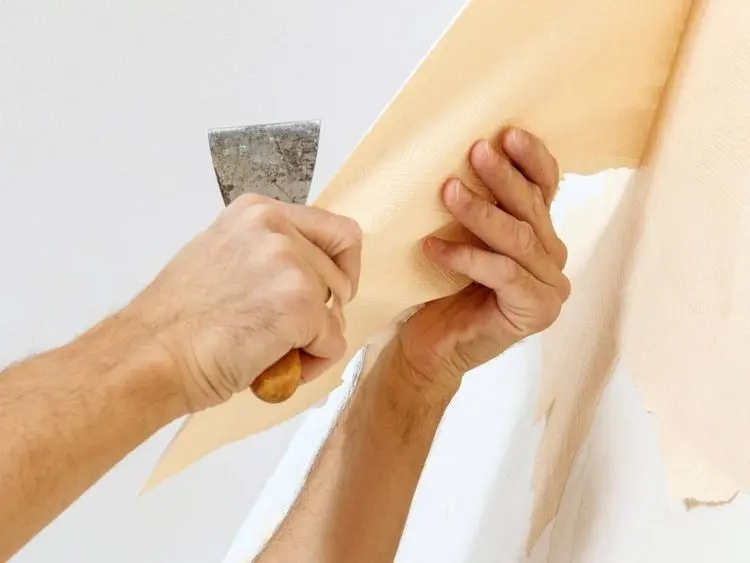 Man in with a scraper in the process of removing old wallpaper.