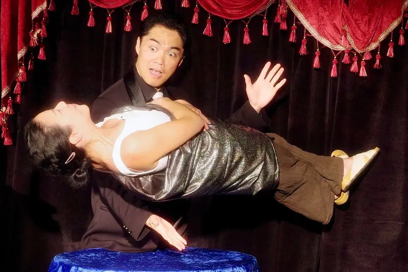 Magician performing a levitation trick with a woman floating above a table, showcasing an illusion during a live performance.