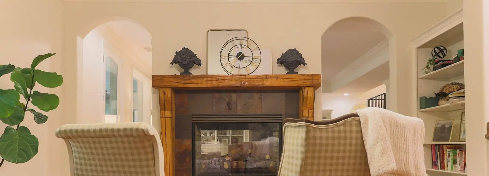 Living room with a wood mantel fireplace between two arched openings and warm white walls.