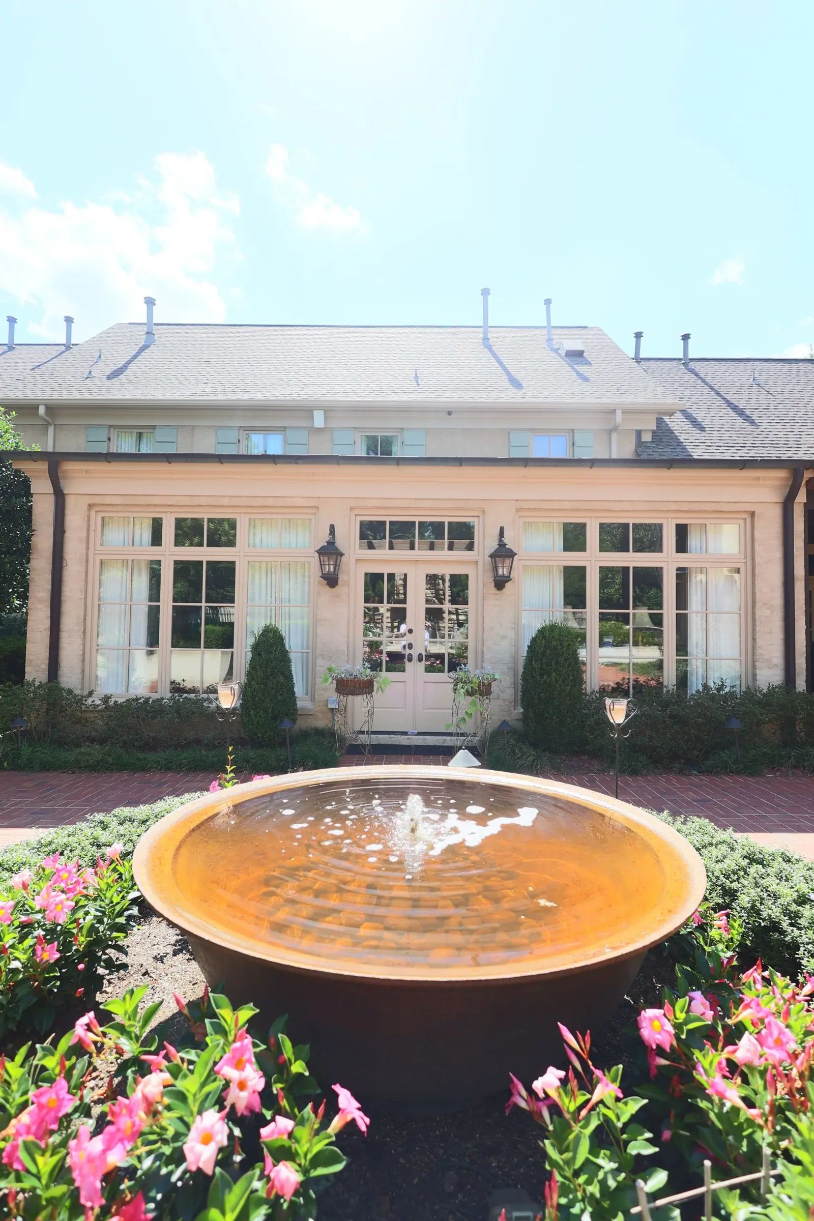 Cream painted brick facade with tall windows behind a copper courtyard fountain.