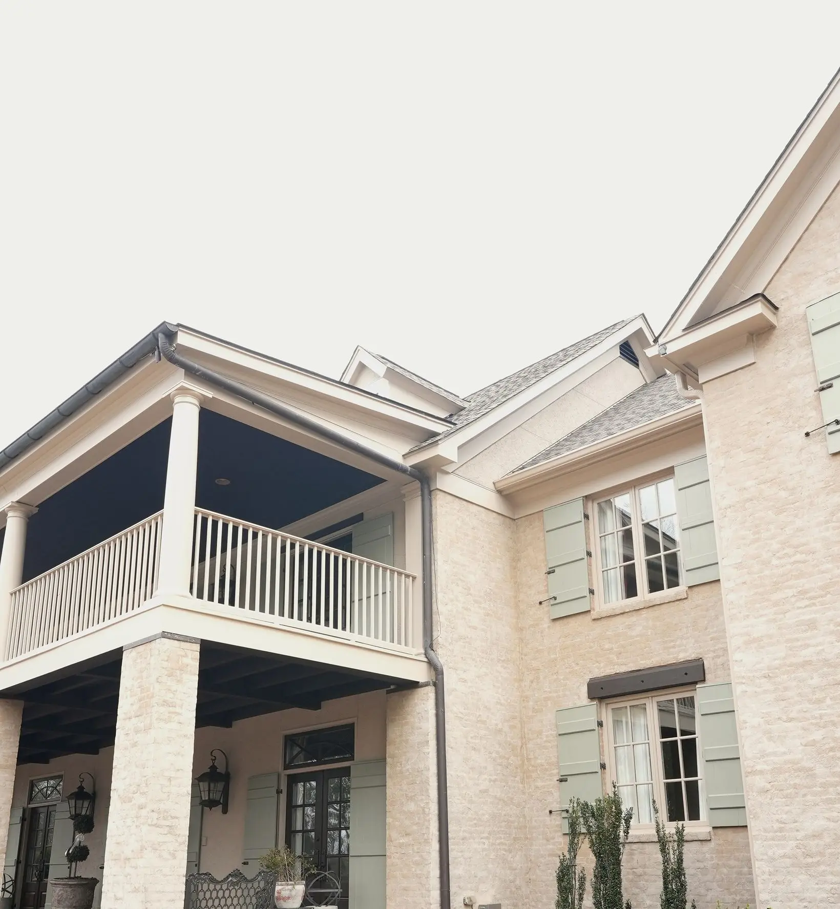 Cream limewash brick house with sage green shutters and a dark porch ceiling.