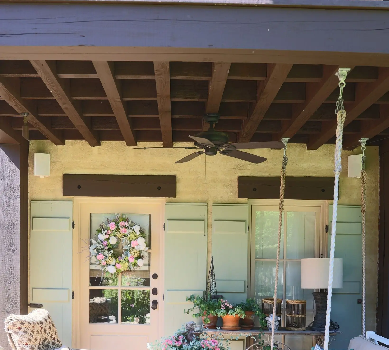 Covered porch with sage green shutters, a pale front door and dark stained ceiling beams.