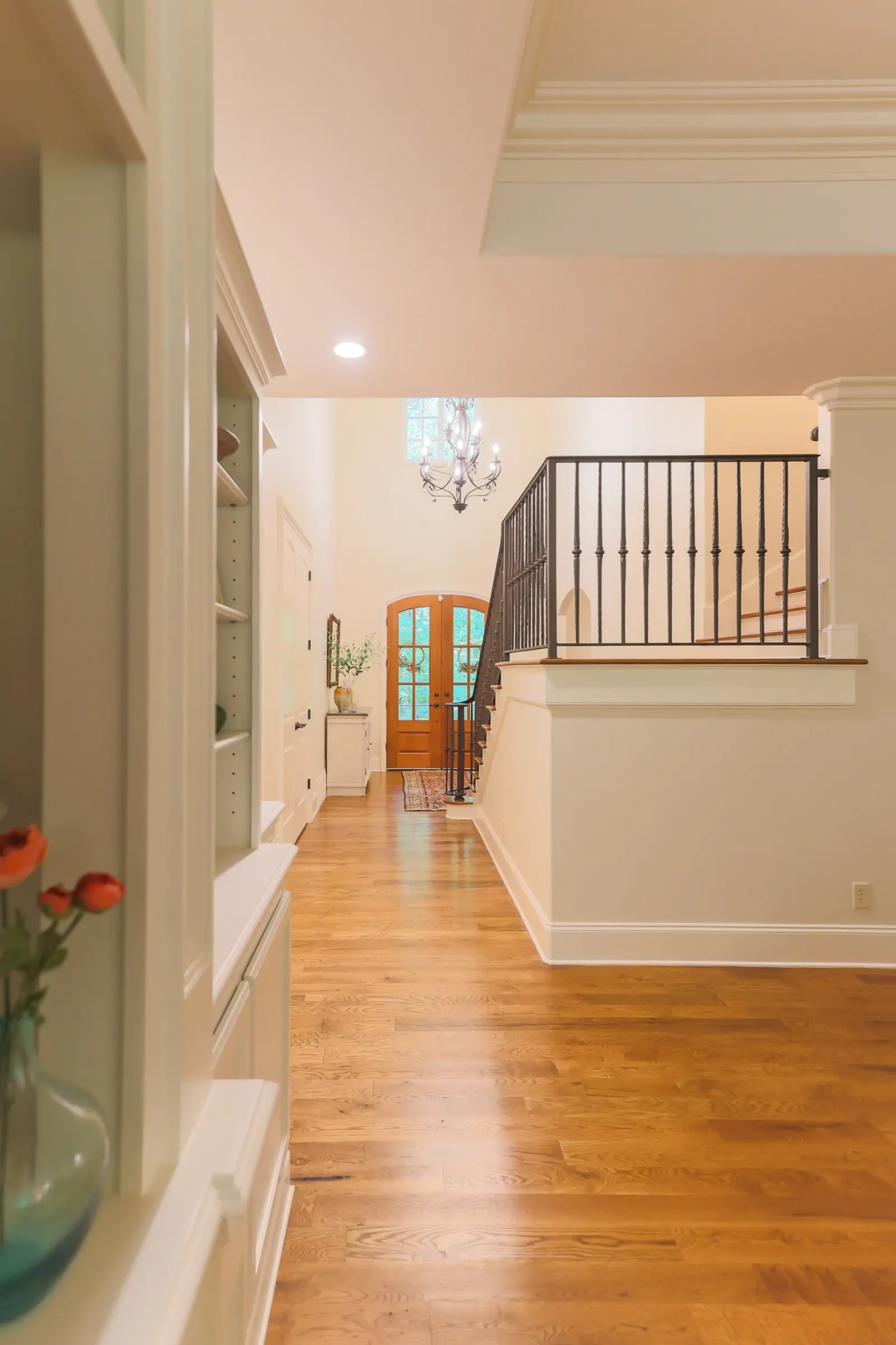 Bright entry hall with cream walls, white trim, wood floors and an iron stair railing.