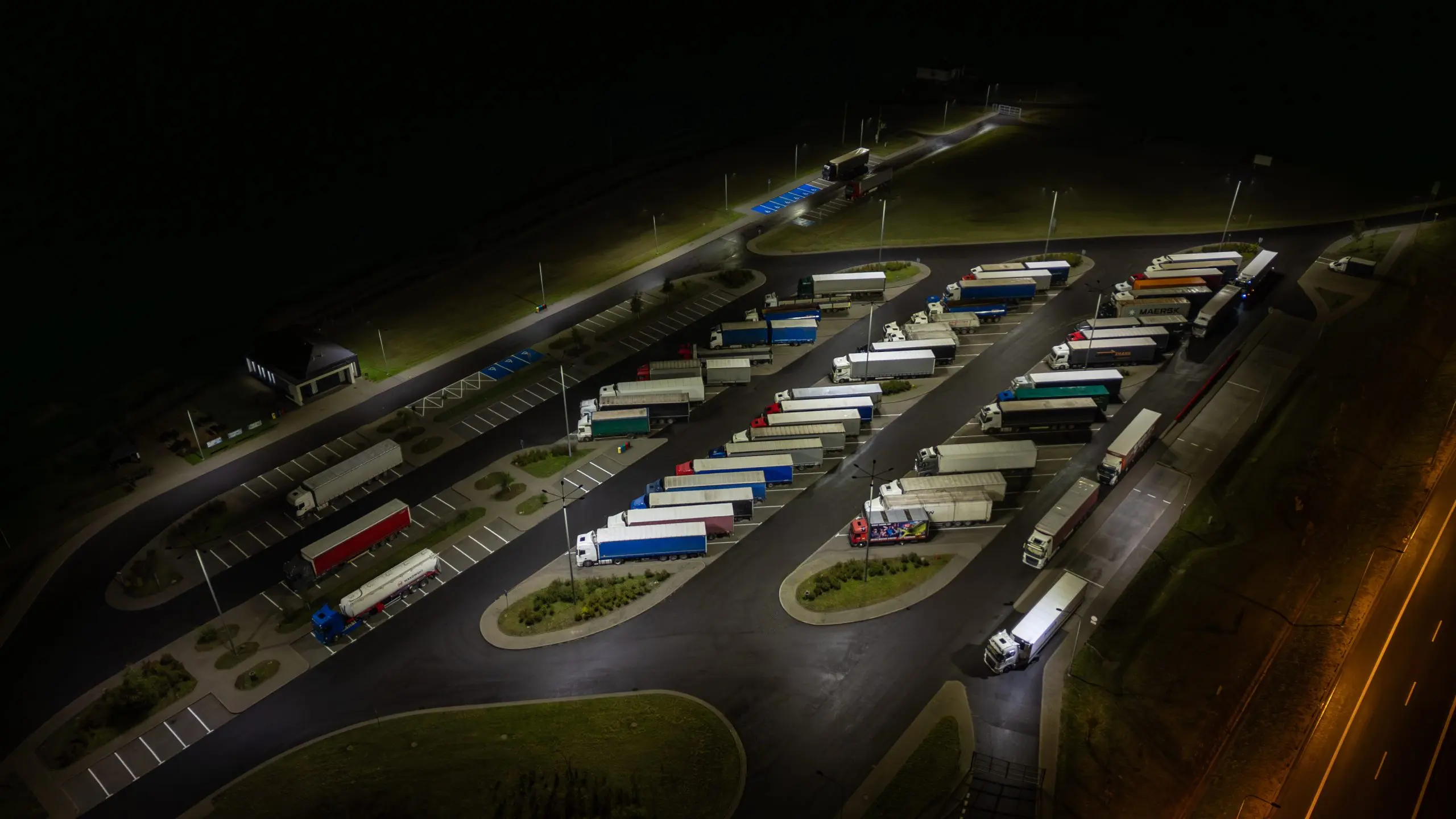 Aerial view of a brightly lit truck stop at night, full of semi-trucks parked for the evening.