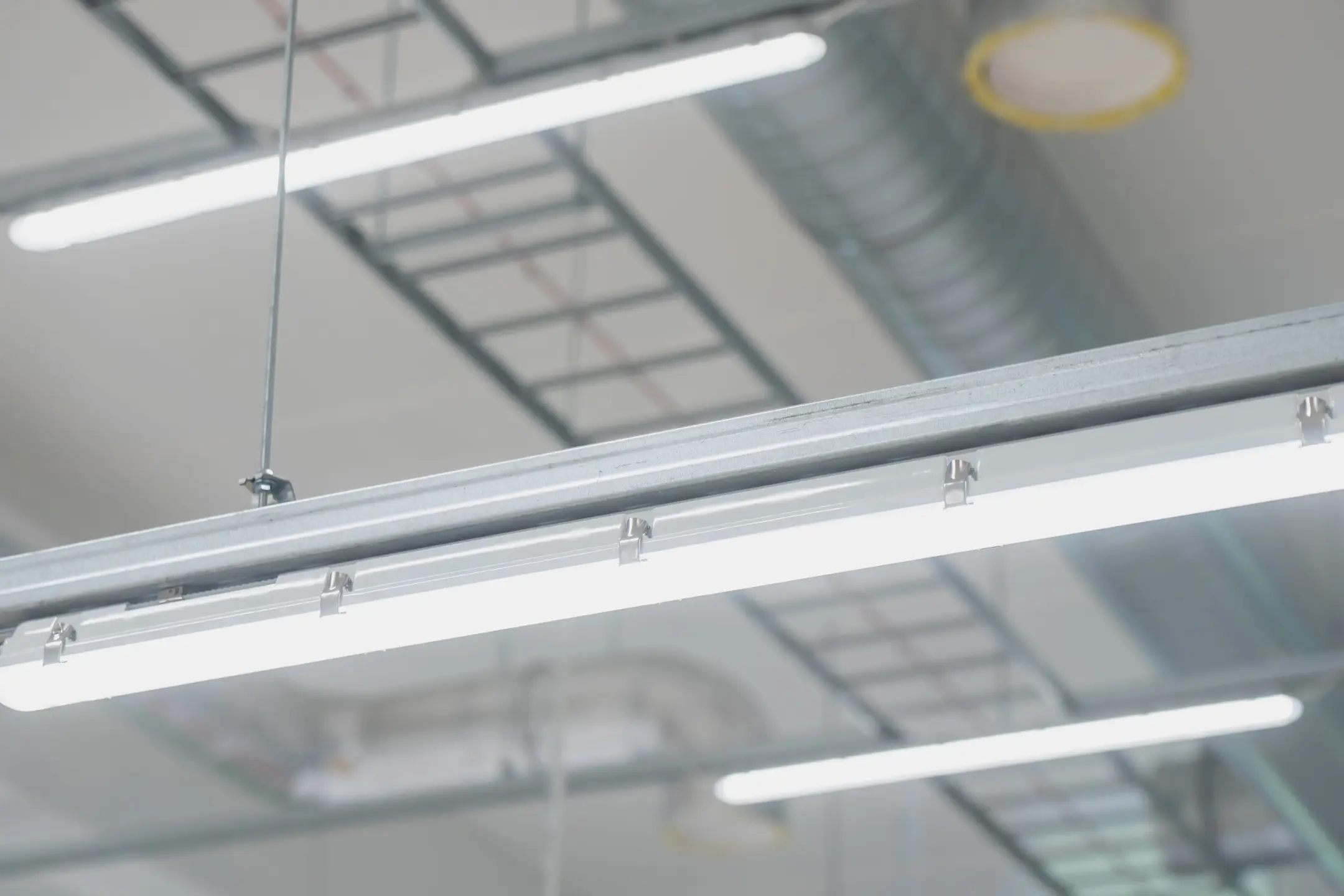 Suspended modular LED lighting fixture with continuous trunking rail installed on a ceiling framework in a modern industrial warehouse