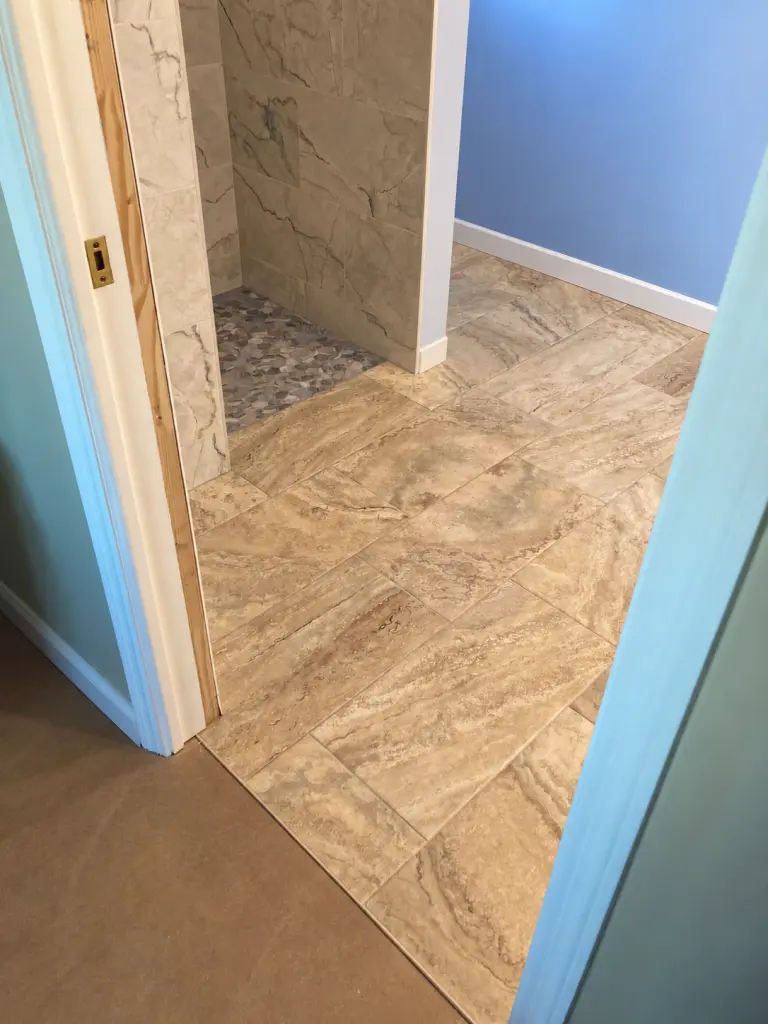 Beige bathroom floor tile beside a blue-gray mosaic shower floor