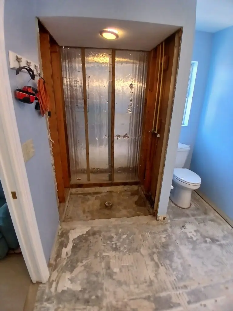 Venice bathroom during demolition, with shower wall framing exposed and old floor tile removed