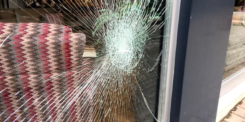 Ventana de vidrio rota con grietas de arañazo, indicando daños de propiedad, relevante para los servicios de Ajustadores Públicos de Santex para ayudar con reclamaciones de seguro.