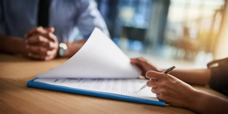Persona que revisa los documentos de seguro y firma papeleo en un entorno profesional, haciendo hincapié en el proceso de asistencia para la liquidación de seguros.