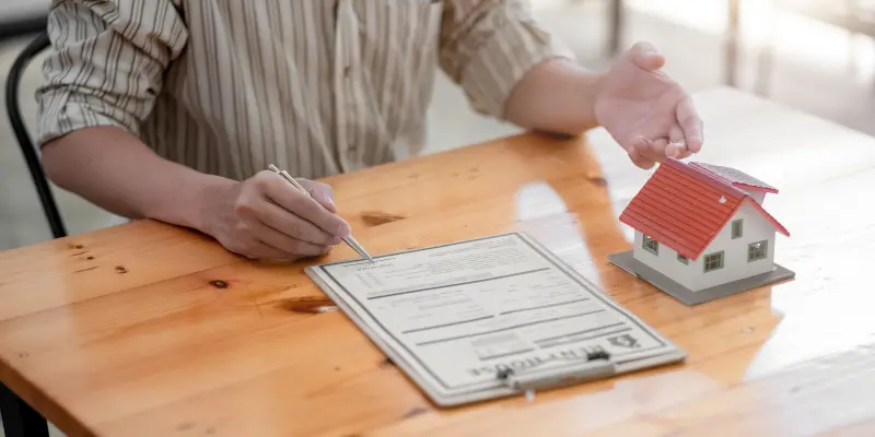 Person discussing home insurance claim details with a model house and paperwork on a wooden table, representing Santex Public Adjusters' services in maximizing insurance settlements.