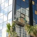 Trabajadores que realizan limpieza exterior en un edificio de alta altura, mostrando esfuerzos de restauración después del daño causado por el agua y la tormenta.
