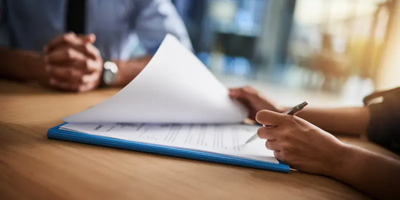 Las manos revisan los documentos de seguro durante una reunión de consulta, haciendo hincapié en la resolución de controversias y la aclaración de políticas.