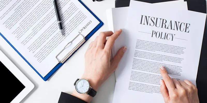 La mano revisa un documento de póliza de seguro sobre un escritorio con papeleo adicional, destacando la importancia de entender las reclamaciones de seguro en Webster, TX.