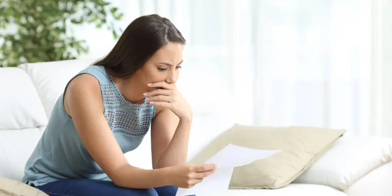 Mujer revisando documentos con una expresión preocupada, reflejando el estrés de tratar con reclamaciones rechazadas del seguro doméstico, relevantes para los servicios de los Ajustadores Públicos de Santex en Houston, TX.
