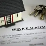 Model house figurine and keys on a service agreement document, symbolizing home insurance claims and recovery processes.