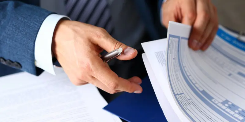 Person in a suit holding documents and a pen, illustrating claims representation and negotiation for insurance services by Santex Public Adjusters.