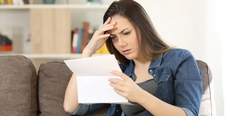 Mujer sentada en un sofá, mirando preocupado mientras leía una carta, reflejando el estrés de tratar con reclamaciones rechazadas del seguro de negocios.