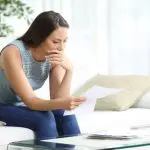 Mujer sentada en un sofá, revisando documentos con una expresión en cuestión, reflejando el estrés de las reclamaciones de seguro de casa denegadas.