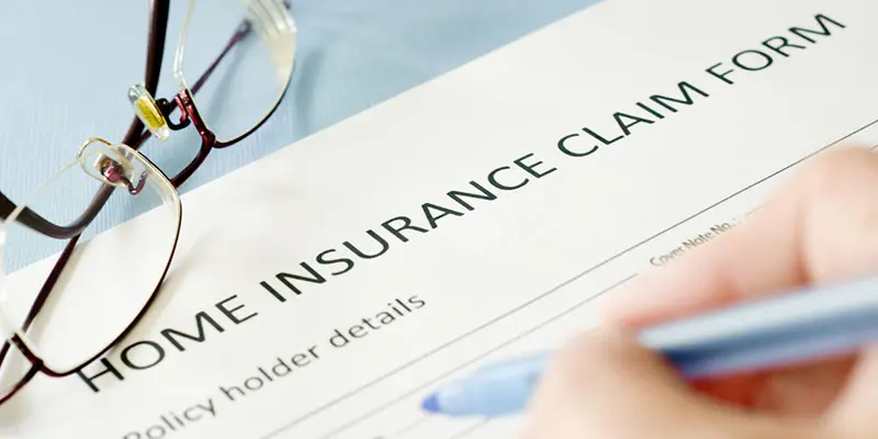 Home insurance claim form withglass and a hand writing, symbolizing the process of filing insurance claims and the services provided by Santex Public Adjusters.