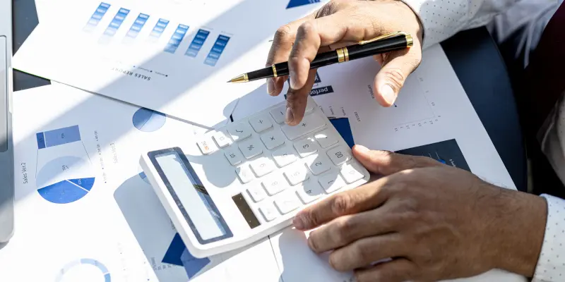 Persona utilizando una calculadora y un bolígrafo sobre documentos financieros, ilustrando el proceso de gestión de reclamaciones y cálculos de seguros para los Ajustadores Públicos de Santex.