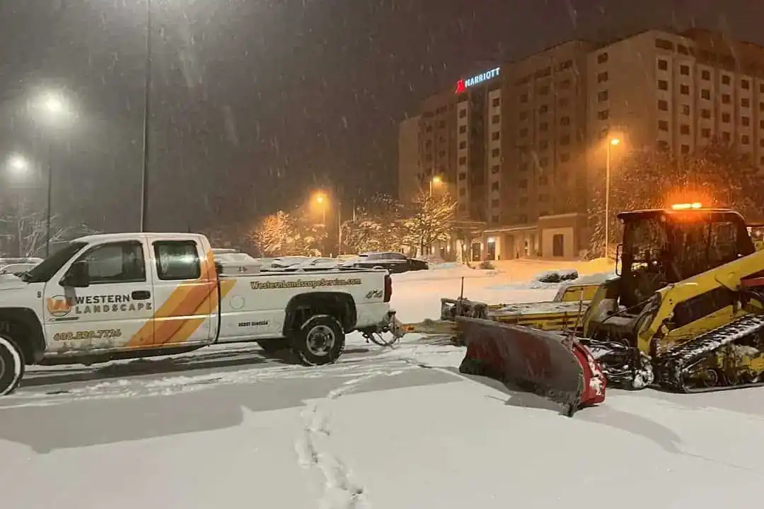 Western Landscape plow truck and skid steer clearing a commercial parking lot during a snowfall
