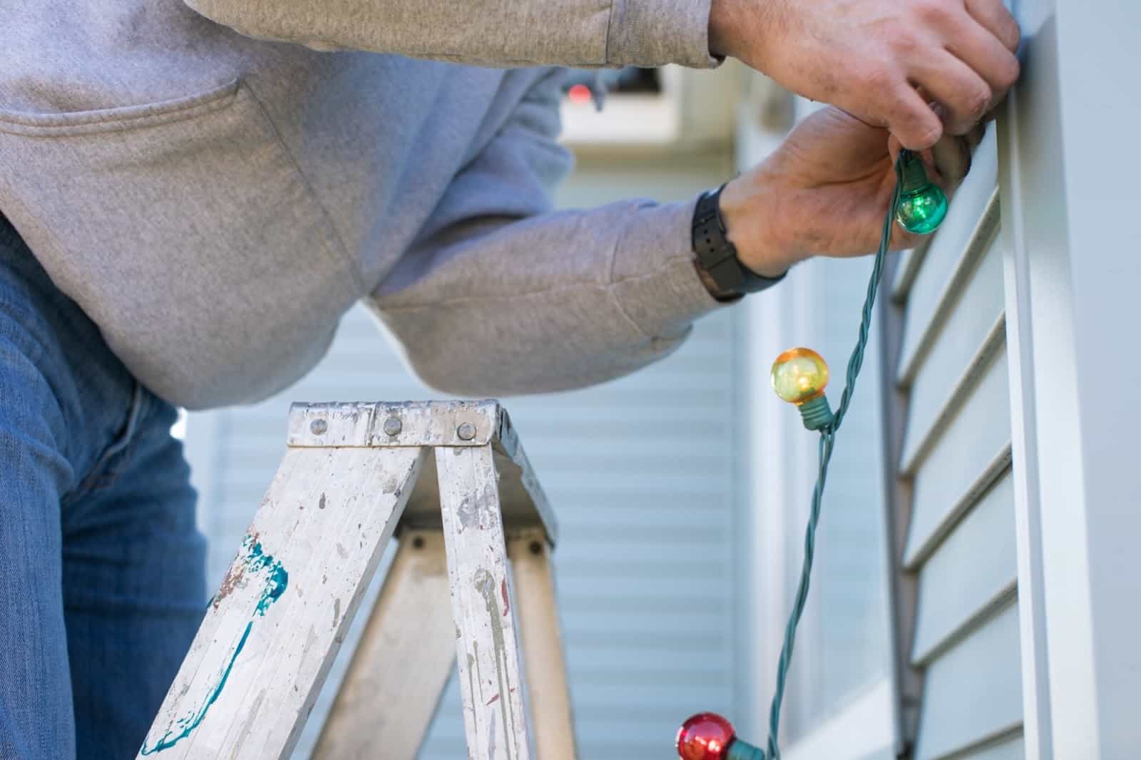 Man Hanging Christmas Lights On House Outside